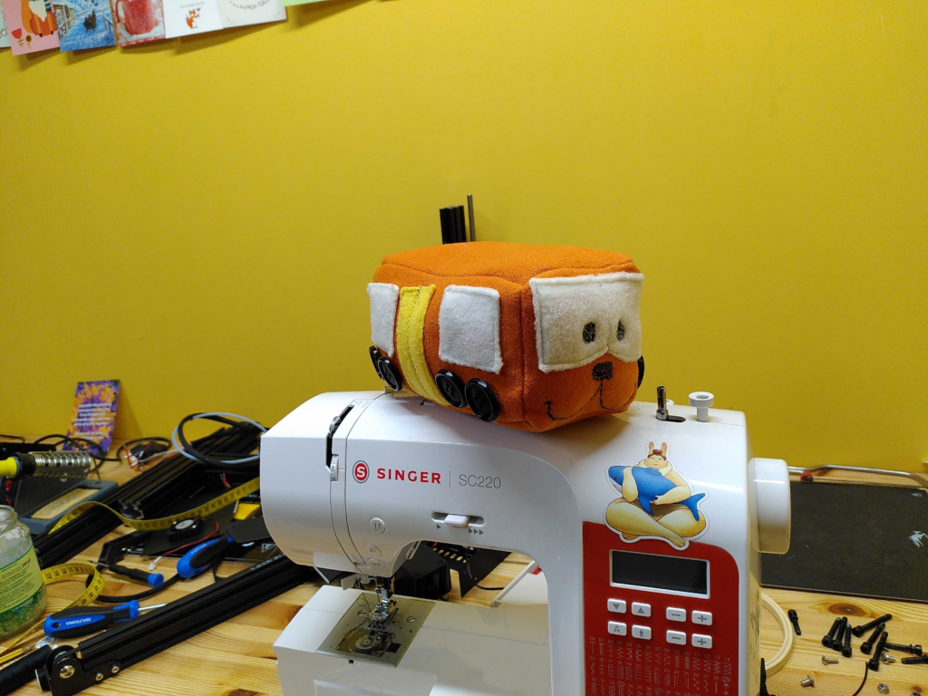 Imogen, the plush train from Immaterial, made in real fabric sitting on top of a sewing machine.